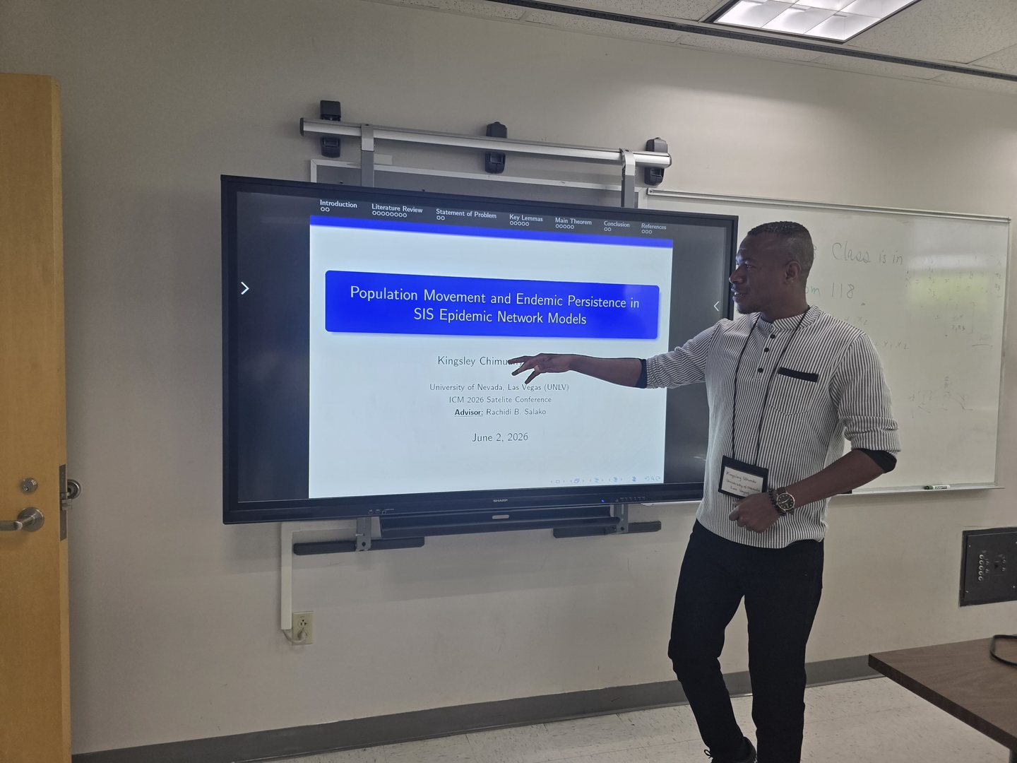 Kingsley presenting his SIS epidemic network research beside a projected presentation slide