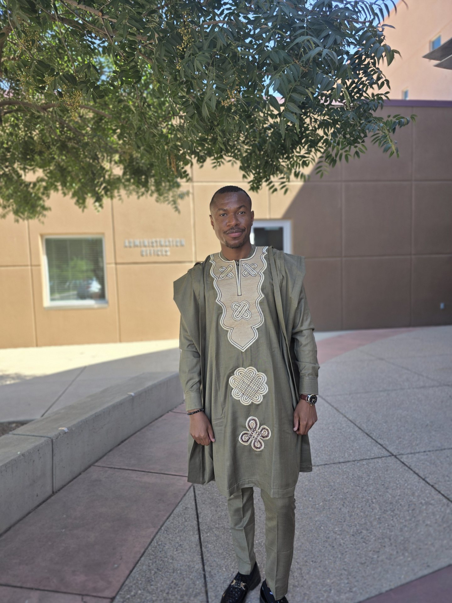 Kingsley seated outdoors in patterned formal attire near water and trees